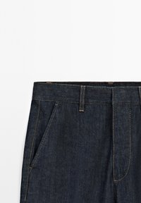 Dark denim trousers featuring a straight cut, traditional five-pocket design, and contrasting yellow stitching along the seams.