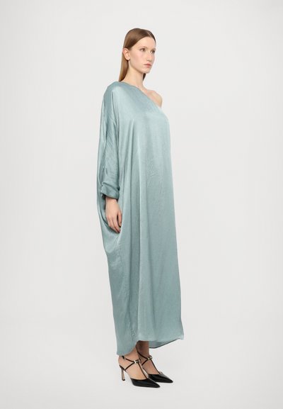 Vestido oversized azul claro hecho de una tela suave, con diseño de un solo hombro. Llevado con tacones negros de punta afilada y accesorios mínimos.