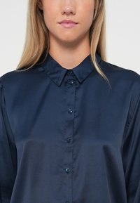 Dark blue satin shirt with a classic collar, front button closure, and smooth texture. Features subtle shine and fitted design.