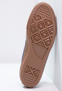 Semelle extérieure en caoutchouc marron d'une sneaker Converse, présentant un motif en losange et un logo en relief. Le bord est légèrement texturé.