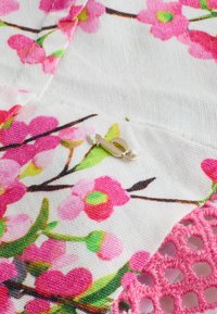 Tissu blanc à imprimé de fleurs de cerisier roses avec un petit fermoir crochet en argent près d'une bordure détaillée en crochet rose.