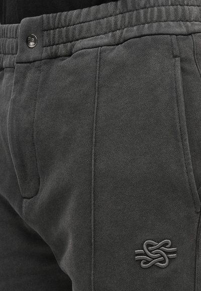 Los pantalones deportivos de color gris oscuro presentan un tejido texturizado, cintura elástica, bolsillos laterales y un parche con logotipo de diseño tejido en el muslo.