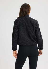 Giacca in pile nera con motivo leopardato, vestibilità rilassata e collettino alto, abbinata a leggings neri. Il tessuto sembra morbido e strutturato.