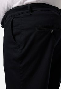 Svarta byxor med en slät yta, figurnära design och bakficka med knappdetalj. Tillverkade av slitstarkt tyg.