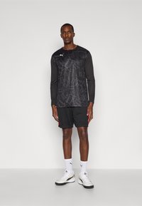Black long-sleeve athletic shirt with geometric pattern, paired with black shorts and white sneakers. White logo on the shirt. Minimalist design.