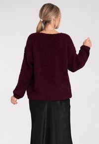 Brązowy, puszysty sweter o luźnym kroju, z prążkowanymi mankietami i okrągłym dekoltem. Zestawiony z czarną elegancką spódnicą, która ma teksturowaną powierzchnię.