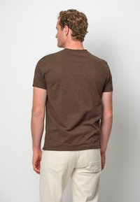 T-shirt marrone a maniche corte con un design classico a girocollo. Il tessuto appare morbido con una texture liscia. Indossato con pantaloni di colore chiaro.