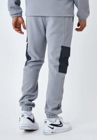 Pantaloni cargo grigi con accenti neri, dotati di tasche laterali e polsini elasticizzati. Il materiale presenta una texture morbida, progettata per il comfort.