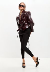 Blazer de charol burdeos con hombreras y cintura ceñida con cinturón, combinada con minifalda negra fruncida y tacones slingback negros.