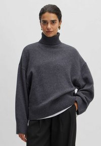 Grau gestreifter Pullover aus weichem Strick mit lockerer Passform, ausgestattet mit gerippten Bündchen und Saum. Dazu schwarze Hose.
