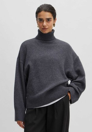 Gray turtleneck sweater in a soft knit with a relaxed fit, featuring ribbed cuffs and hem. Paired with black trousers.
