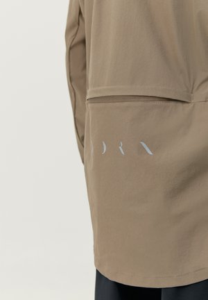 Hnedá ľahká bunda s hladkým povrchom, bočnou vreckom a reflexným logom na chrbte. Klasický dizajn, dĺžka po kolená.