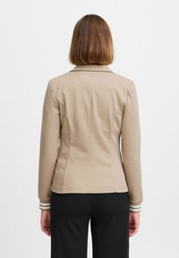 Beige taillierte Jacke mit Kragen, Ein-Knopf-Verschluss und gestreiften Manschettendetails. Glattes Material und maßgeschneiderter Schnitt.