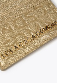Tarjetero texturizado en oro con logo en relieve y letras en tono dorado. Cuenta con una superficie lisa y bordes cosidos para mayor durabilidad.