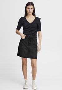 Jupe en denim noir à coupe droite, avec une taille haute et une fermeture à boutons à l'avant, associée à un haut noir à côtes ajusté.