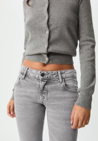 Grå kardigan med knappstängning och långa ärmar, tillsammans med figurnära grå jeans med femficksdesign och subtil textur.