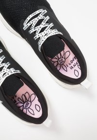 Černé pletené běžecké boty s bílými tištěnými tkaničkami, růžovými vnitřními solemi s květinovým vzorem a textem. Gumená podrážka s poutkem na patě.