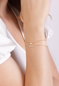 Gold chain bracelet featuring two rows with a round stone and a line of small stones, worn on a wrist against a light background.