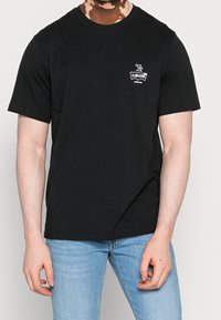 Černé bavlněné tričko s krátkým rukávem, kulatým výstřihem a malým bílým logem Levi's na hrudi, v kombinaci se světle modrými džíny.