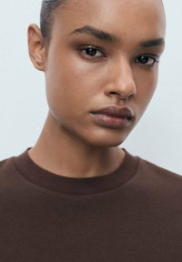 Brown short-sleeved t-shirt with a round neckline, displayed on a model. Smooth fabric texture, neutral background enhancing the garment.