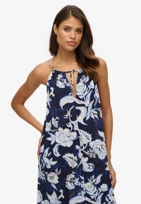 Vestido navy con estampado floral blanco, diseño de cuello halter, abertura en forma de ojo de cerradura, tejido ligero y silueta fluida.