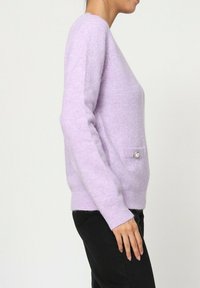 Pull en tricot lilas clair avec une coupe décontractée, doté de manches longues, de poignets côtelés et d'une petite poche à boutons sur le devant.