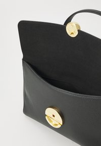 Sac à main en cuir noir avec une texture lisse, doté d'un fermoir circulaire doré et d'une seule poignée supérieure. L'intérieur présente une doublure sombre.