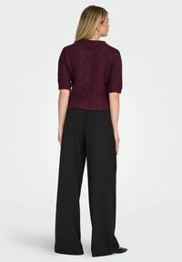 Maglia bordeaux a maniche corte con scollo rotondo e vestibilità ampia, abbinata a pantaloni neri a gamba larga e vita alta.