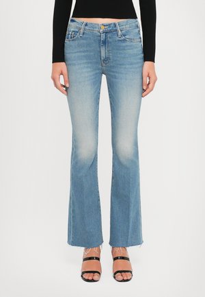 Jeans acampanados de denim azul claro con un acabado desgastado, cinco bolsillos, un sutil arrugado y un dobladillo sin terminar. Combinados con sandalias negras de tiras.