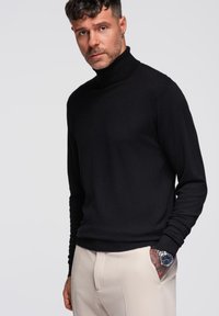 Czarny sweter typu golf wykrojony z cienkiej dzianiny, z długimi rękawami i luźnym krojem. Połączony z jasnymi spodniami.