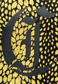 Μαύρο αφηρημένο γοτθικό γράμμα "G" που επικαλύπτει ένα φόντο υφάσματος με κίτρινο και μαύρο σχέδιο λεοπάρδαλης.