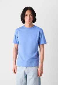 Lys blå bomull T-skjorte med rund hals, korte ermer, subtil logo detalj på brystet og avslappet passform. Kombinert med lyse denimjeans.