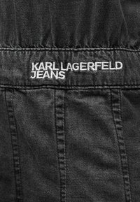 Το μαύρο τζιν ύφασμα διαθέτει ραφές με διακοσμητική ραφή και ένα κεντημένο λευκό λογότυπο που αναγράφει "KARL LAGERFELD JEANS" στη μέση.