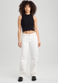 Black ribbed knit cropped tank top paired with high-waisted white straight-leg jeans and black chunky shoes. Plain background.