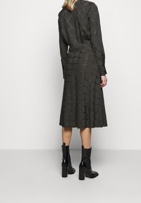 Vestido verde oscuro con un patrón de rombos texturizado, mangas largas y falda acampanada, combinado con botas negras brillantes de tacón cuadrado.