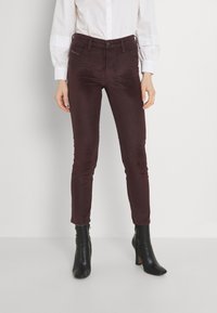 Burgundské slim-fit kalhoty vyrobené z jemné látky, s kapsami a knoflíkovým zapínáním v pase, v kombinaci s černými kotníkovými botami na podpatku.