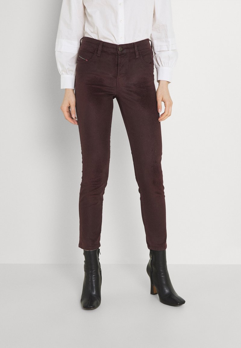 Burgundské slim-fit kalhoty vyrobené z jemné látky, s kapsami a knoflíkovým zapínáním v pase, v kombinaci s černými kotníkovými botami na podpatku.