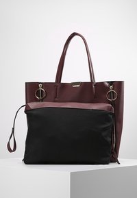 Sac à main bordeaux et noir avec un extérieur en cuir texturé, deux poignées, et une pochette en tissu noire amovible avec fermeture éclair.