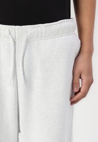 Lysegrå sweatpants med elastisk talje, snøre detaljer og et blødt, tekstureret stof; hånd hvilende på siden.