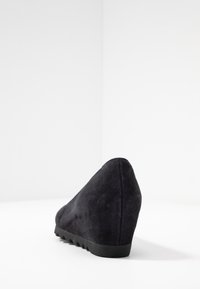 Chaussure à talon compensé en daim noir avec un bout pointu, une surface texturée et une semelle en caoutchouc striée. Présentée sous un angle arrière.