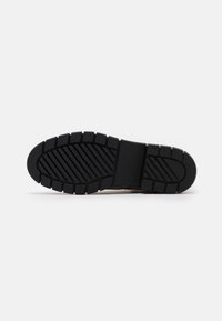 Suela de zapato de goma negra con un patrón texturizado y acanalado, y relieve en la banda para mayor agarre; tacón plano, redondeado y área de soporte central del arco.