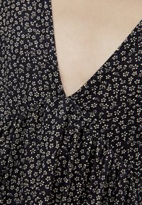 Czarna sukienka w kwiaty z głębokim dekoltem w kształcie litery V, z marszczeniem w talii i małymi białymi wzorami kwiatowymi na granatowym tle.