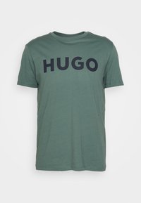 Zelené bavlněné tričko s kulatým výstřihem a krátkými rukávy. Na přední straně je velký černý potisk "HUGO".