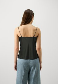 Camisola nera in satin con spalline sottili regolabili, caratterizzata da un scollo dritto e un taglio fluido, abbinata a pantaloni larghi blu chiaro.