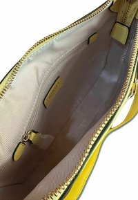 Borsa gialla con zip dorata, dotata di un interno foderato beige. Include tasche interne e una texture liscia con bordi verdi a contrasto.