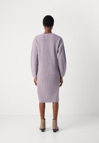 Ceriņu krāsas adīta kleita ar ribotu tekstūru, garām bumbierveida piedurknēm un potītei līdzīgu garumu. Tajā ir apaļa kakla izgriezne un smalka aizmugures apdare.