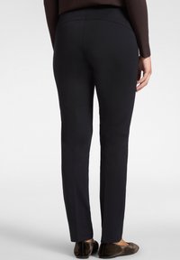 Zwarte stretchbroeken met een gladde textuur, met een getailleerd ontwerp en elastische tailleband, eindigend net boven de enkel, gecombineerd met donkere flats.