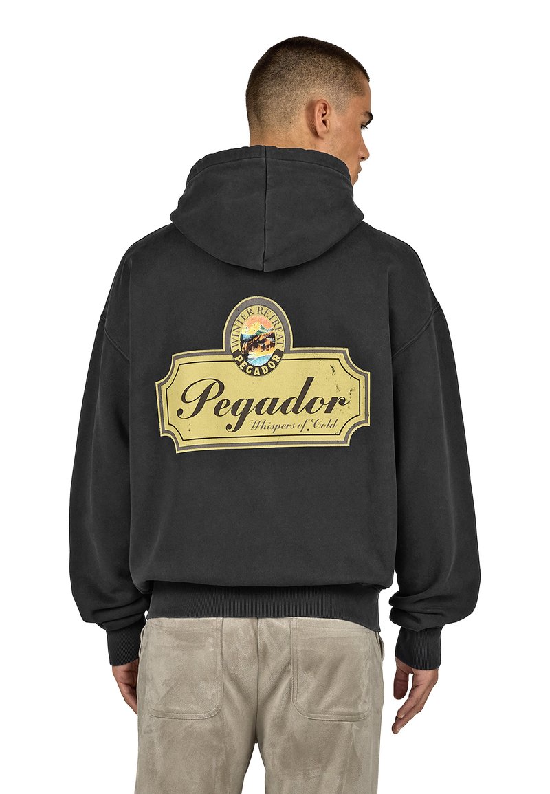 Juodas su kapucija džemperis su dideliu retro stiliaus geltonu logotipu, ant nugaros esantu rašmeniu "Pegador", vaizduojančiu kalnų peizažą ir tekstūruotu audiniu.