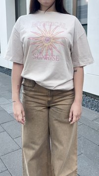 Camiseta bege de mangas curtas com um gráfico de sol, combinada com calças castanhas de perna larga, ambas com tecido suave e um corte casual.
