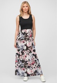 Robe maxi avec un haut sans manches noir et une jupe à motifs floraux en rose, blanc et bleu sur fond sombre. Portée avec des baskets blanches.
